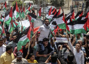 Palestinians wave national flags during a protest in Khan Yunis town in the southern Gaza Strip over tensions in Jerusalem’s Al-Aqsa Mosque as Israelis mark Jerusalem Day, on May 29, 2022. – Jerusalem is bracing for a controversial “flag march” by Israelis that has sparked warnings of a new escalation from Palestinian factions. (Photo by SAID KHATIB / AFP)