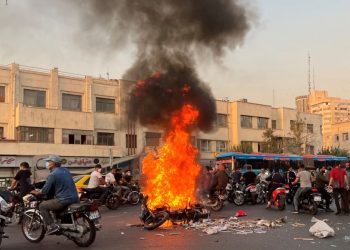 A picture obtained by AFP outside Iran, shows people gathering next to a burning motorcycle in the capital Tehran on October 8, 2022. – Iran has been torn by the biggest wave of social unrest in almost three years, which has seen protesters, including university students and even young schoolgirls chant “Woman, Life, Freedom”. (Photo by – / AFP)