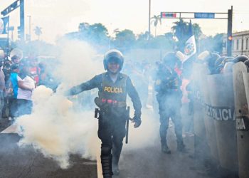 A police officer throws smoke while people protest against the government of Peruvian President Dina Boluarte in Lima on January 17, 2023. – Peruvian President Dina Boluarte asked this Tuesday to the hundreds of protesters from various regions of the country who are heading to Lima to protest against their government to do so in “peace and calm.” (Photo by ERNESTO BENAVIDES / AFP)