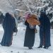 (FILES) In this file photo taken on January 23, 2023, Afghan burqa-clad women carry children as they walk along a snow laden street in Kabul. – At least 166 people have perished in a wave of bitterly cold weather sweeping Afghanistan, officials said January 28, as extreme conditions continue to heap misery on the poverty-stricken nation. (Photo by Wakil KOHSAR / AFP)