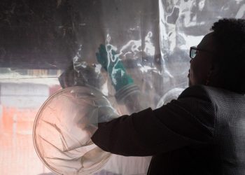 (FILES) In this file photo taken on December 09, 2022, Uganda’s Health Minister Jane Ruth Aceng tries to use the gloves through the transparent medical intervention wall at the newly installed makeshift Ebola Treatment Unit with 32 beds, also to be used as a research centre for Ebola strains and vaccine trial, in Kampala. – Uganda on January 11, 2023 declared an end to an outbreak of the deadly Ebola virus that emerged late last year and claimed the lives of 55 people, the World Health Organization and the country’s health minister said. (Photo by Badru KATUMBA / AFP)