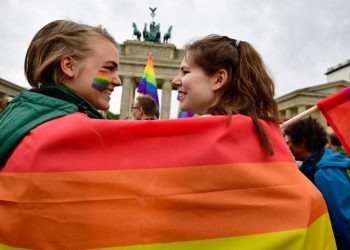 (FILES) In this file photo taken on June 30, 2017 two women are wrapped into a rainbow flag as they attend a rally of gays and lesbians in front of the Brandenburg Gate in Berlin. The same-sex partners of EU citizens have the right to live in any member state whatever their nationality, the bloc’s top court ruled on June 5, 2018, even in countries that do not recognise gay marriage. “Although the Member States have the freedom whether or not to authorise marriage between persons of the same sex, they may not obstruct the freedom of residence of an EU citizen by refusing to grant his same-sex spouse, a national of a country that is not an EU Member State, a derived right of residence in their territory,” the court said./ AFP PHOTO / Tobias SCHWARZ