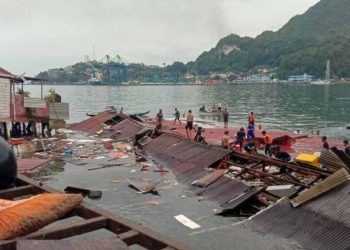 People stand on the roofing of collapsed shops in the port after a 5.1-magnitude earthquake in Jayapura, Indonesia’s eastern province of Papua on February 9, 2023. (Photo by FAISAL NARWAWAN / AFP)