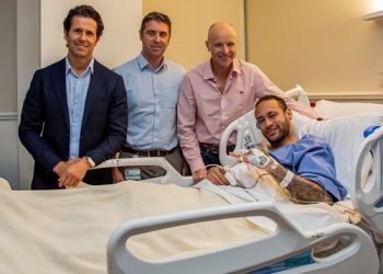 This handout picture provided by Aspetar Hospital in Doha on March 10, 2023 shows Paris Saint-Germain’s Brazilian forward Neymar da Silva Santos Junior (R) gesturing in bed after after undergoing surgery at the facility, accompanied by the hospital’s Chief Medical Officer Dr Pieter D’Hooghe (2nd-L), ankle surgeon Dr Pierre James Calder (2nd-R), and Brazilian surgeon and national team doctor Rodrigo Lasmar (L).