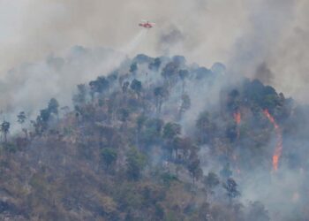 This photograph taken on March 30, 2023 shows a helicopter dropping water over a forest fire hotspot on Khao Laem mountain in Nakhon Nayok province, northeast of Bangkok. (Photo by Panumas SANGUANWONG / THAI NEWS PIX / AFP)