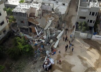 In this aerial view, people gather in front of a building hit by an Israeli air strike, in Gaza city on May 13, 2023. – Israel and Gaza traded heavy fire on May 12 but Egyptian mediators launched a new bid to end days of fighting that has killed dozens, all but one of them Palestinian. (Photo by MAHMUD HAMS / AFP)