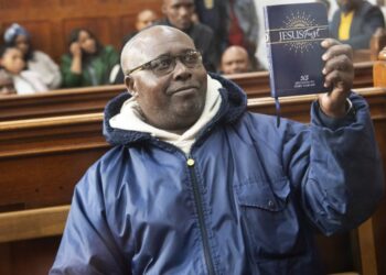 Fulgence Kayishema, one of the last fugitives sought for their role in the 1994 Rwanda genocide, holds up a Christian book as he sits in the Cape Town Magistrate’s Court in Cape Town on May 26, 2023, two days after being arrested following 22 years on the run. (Photo by RODGER BOSCH / AFP)