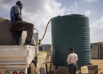 A woman waits for a jars to be filled with water from a tank in an informal settlement in Hammanskraal on May 23, 2023. – An outbreak of cholera has killed at least 15 people near South Africa’s capital of Pretoria, as city officials urged residents of Hammanskraal and surrounding areas not to drink from the tap, adding water tankers were being supplied. Cholera has experienced a global resurgence since 2021 after a decade of steady decline, according to the United Nations, which this week warned one billion people in 43 countries were at risk. The disease is not endemic in South Africa. (Photo by Michele Spatari / AFP)