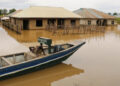 A man rests on a boat next to flooded houses following heavy rain.