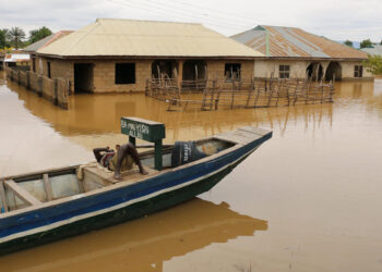 A man rests on a boat next to flooded houses following heavy rain.