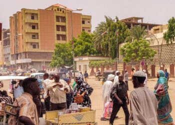 Pedestrians and vehicles move along a road outside a branch of the Central Bank of Sudan in the country’s eastern city of Gedaref on July 9, 2023. – Many civil servants in Sudan have been going on without a salary since the Sudanese army and the paramilitary Rapid Support Forces took up arms against each other. (Photo by – / AFP)