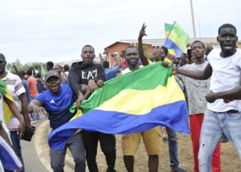 Residents gesture and hold a Gabon national flag as they celebrate in Libreville on August 30, 2023 after a group of Gabonese military officers appeared on television announcing they were “putting an end to the current regime” and scrapping official election results that had handed another term to veteran President Ali Bongo Ondimba. – In a pre-dawn address, a group of officers declared “all the institutions of the republic” had been dissolved, the election results cancelled and the borders closed. (Photo by – / AFP)