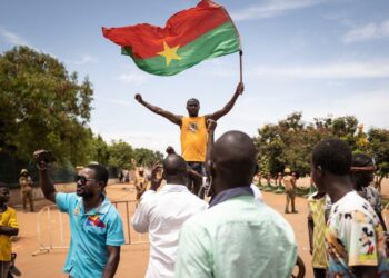 A man waves a Burkina Faso flag as others demonstrate while Burkina Faso soldiers are seen deployed in Ouagadougou on September 30, 2022. – Shots rang out before dawn on Friday around Burkina Faso’s presidential palace and headquarters of the military junta, which itself seized power in a coup last January. The government said the developing situation was linked to an “internal crisis in the army”, after AFP journalists saw troops block several main roads in the capital Ouagadougou. (Photo by Olympia DE MAISMONT / AFP)