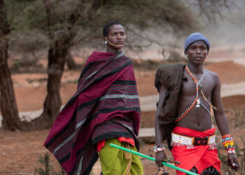 Lisoka Lesasuyan (L), 21, is led by his brother, Joshua as they walk along a dirt road after contact with a piece of unexploded military ordnance in 2013 left Lisoka a double-amputee whose lost both his arms, partially blind and deaf, at Kipsing village, Isiolo county on October 18, 2023. (Photo by Tony KARUMBA / AFP)