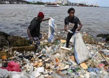 (FILES) Residents collect plastics bottles and bags in the Ebrie Lagoon in Abidjan on May 31, 2023 ahead of World environnement Day celebrations. – The latest negotiations towards a global treaty to combat plastic pollution open in Nairobi on November 13, 2023 with tensions expected as nations tussle over what should be included in the pact.Some 175 countries agreed last year to conclude by 2024 a UN treaty to combat the plastic blighting oceans, floating in the atmosphere and infiltrating the bodies of animals and humans. (Photo by Issouf SANOGO / AFP)