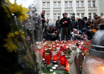 People place flowers and candles at a makeshift memorial for the victims outside the Charles University in central Prague, on December 22, 2023, as police investigators kept working on the campus the day after a deadly mass shooting. – Czech police said the December 21, 2023 shooting at Prague’s Charles University left 14 dead and 25 wounded, revising down a previously announced toll of more than 15 victims.”At this moment I can confirm 14 victims of the horrible crime and 25 wounded, of which 10 seriously,” police chief Martin Vondrasek told reporters. (Photo by Michal CIZEK / AFP)