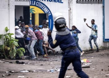 A Police officer throws a rock as opposition supporters run into a opposition leader Martin Fayulus party house during a demonstration in Kinshasa on December 27, 2023. - Police were deployed in the Democratic Republic of Congo's capital Kinshasa on December 27, 2023 during a banned demonstration against recent elections in the fragile central African state.Leading opposition politicians in impoverished but mineral-rich DRC have rejected last week's vote, which was marred by severe delays and bureaucratic disarray, and called for a demonstrations. (Photo by JOHN WESSELS / AFP)