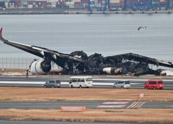 Officials look at the burnt wreckage of a Japan Airlines (JAL) passenger plane on the tarmac at Tokyo International Airport at Haneda in Tokyo on January 3, 2024, the morning after the JAL airliner hit a smaller coast guard plane on the ground. – Five people aboard a Japan coast guard aircraft died on January 2 when it hit a Japan Airlines passenger plane on the ground in a fiery collision at Tokyo’s Haneda airport. (Photo by Richard A. Brooks / AFP)