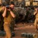 Israeli soldiers carry heavy shells past battle tanks deployed at a position along the border with the Gaza Strip and southern Israel on December 31, 2023, amid the ongoing conflict between Israel and the militant group Hamas. (Photo by Menahem KAHANA / AFP)