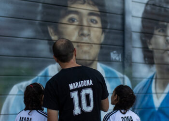 Walter Rotundo (C) poses for a photo with his twins daughters Mara (L) and Dona, named in honour of the football star Diego Maradona, in front of murals painted outside of Diego Maradona stadium in Buenos Aires, on November 16, 2021. A 39-year-old Argentinian, a Diego Maradona fanatic like millions of his compatriots, became the proud father of a little “Diego” on the anniversary of the idol’s death. In a few days, he will join his two 10-year-old sisters, named Mara, and Dona. TOMAS CUESTA / AFP